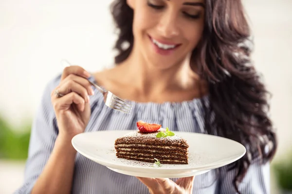女性がフォークをかけた上に苺とミントの葉がのった層状のブラウン色の白いケーキ — ストック写真