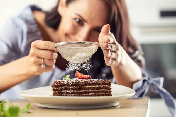 女性はスライスした層状ケーキの上に粉砂糖を振りかける — ストック写真