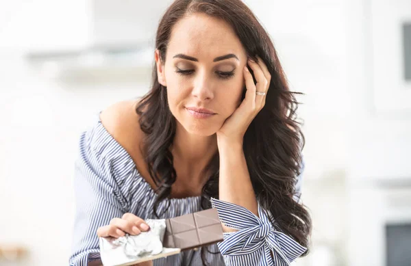 Woman thinks whether to eat or not to eat an unpacked bar of chocolate.