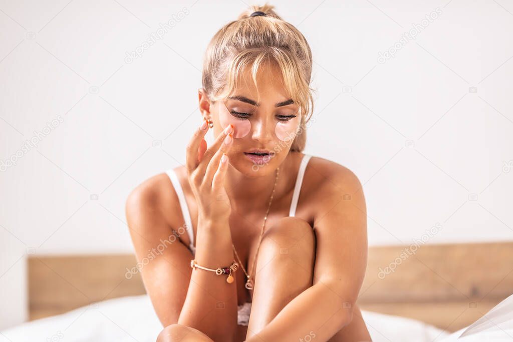Young caucasian female applies eye pads to ease swollen skin.