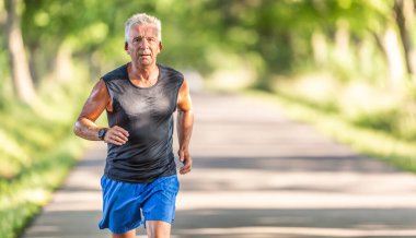 Şortlu ve gömleksiz formalı yaşlı bir adam doğada koşar..