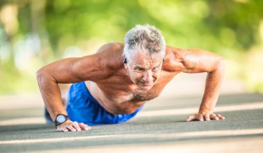 Güneşli bir yaz gününde yolda şınav çeken yaşlı bir adam..