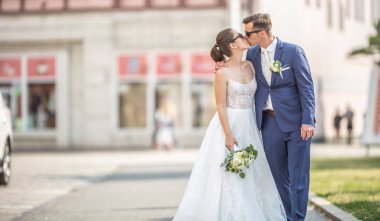 Beautiful couple kissing each other in the middle of the town. They  are just married and are having a photo taken to the album.