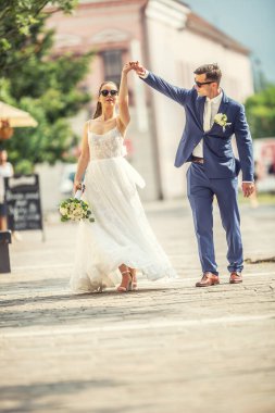 A groom dancing with her bride in the town after a wedding. Still wearing beautiful robes and holding a bouquet made of white flowers.,