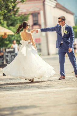 A groom dancing with her bride in the town after a wedding. Still wearing beautiful robes and holding a bouquet made of white flowers.,