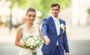 Charming couple holding eeach others hand while wanking in the town. They are wearing wedding robes and holding nice flowers.