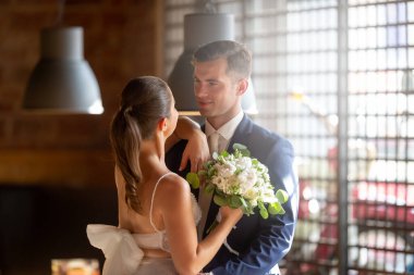 Elegant couple is having a photo taken in the restaurant after the ceremony. Wedding robes and delightful bouquet.