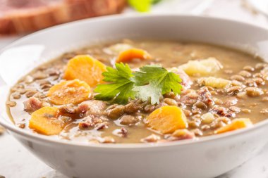 Lentil soup with pieces of smoked pork neck, carrots, potatoes and coriander. Traditional Slovak, Czech or Eastern European food.