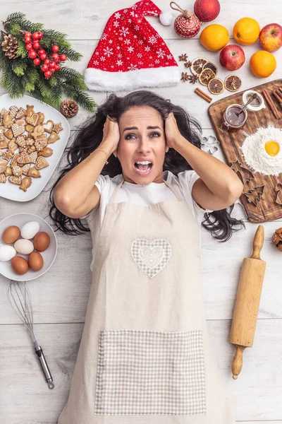 满头黑发的厨师头脑发热 躺在地上 四周都是姜汁 木制桌子上的面粉 圣诞帽 晒干的橙子和烘培的面包 — 图库照片