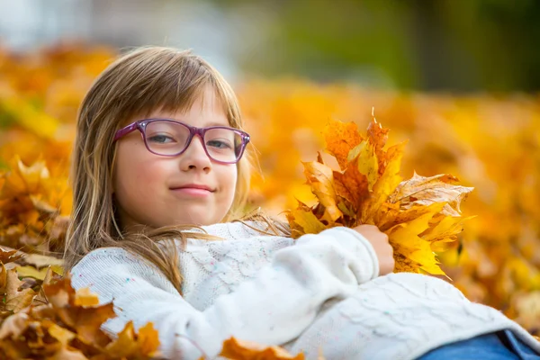 Young girl lying on the colored maple leaves in hands holding a bouquet from the same leaves — Stock Photo, Image