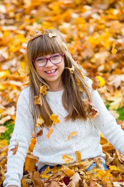 Portrait of a smiling young girl who is holding in her hand a bouquet of autumn maple leaves.Girl sitting on colorful autumn leaves. — Stock Photo, Image