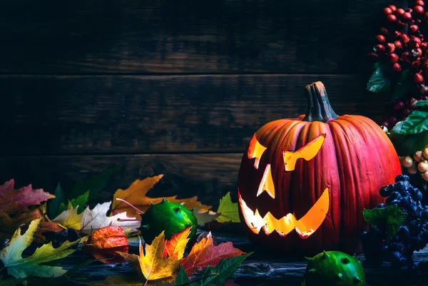 Jack o lanternas Halloween rosto de abóbora no fundo de madeira e folhas de outono — Fotografia de Stock