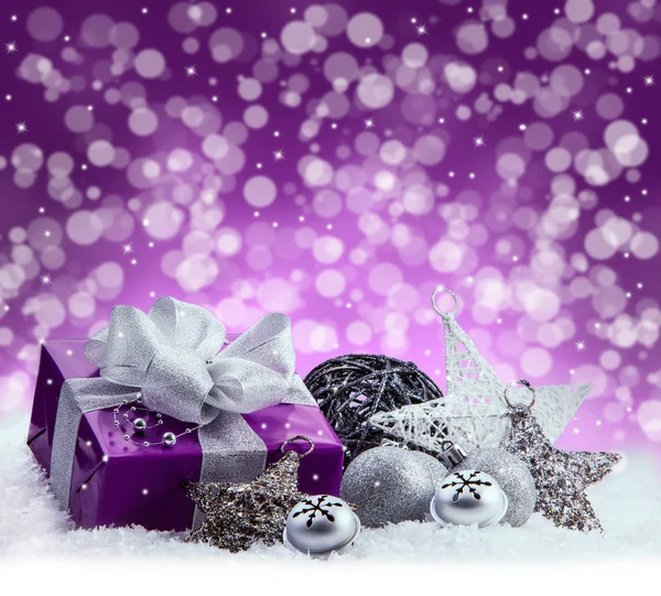 Fialová vánoční balíček, dar stříbrná stuha. Rolničky, stříbrné vánoční koule a vánoční hvězdy na sněhu. Vícebarevné rozostřeného pozadí abstraktní prostor. Royalty Free Stock Fotografie