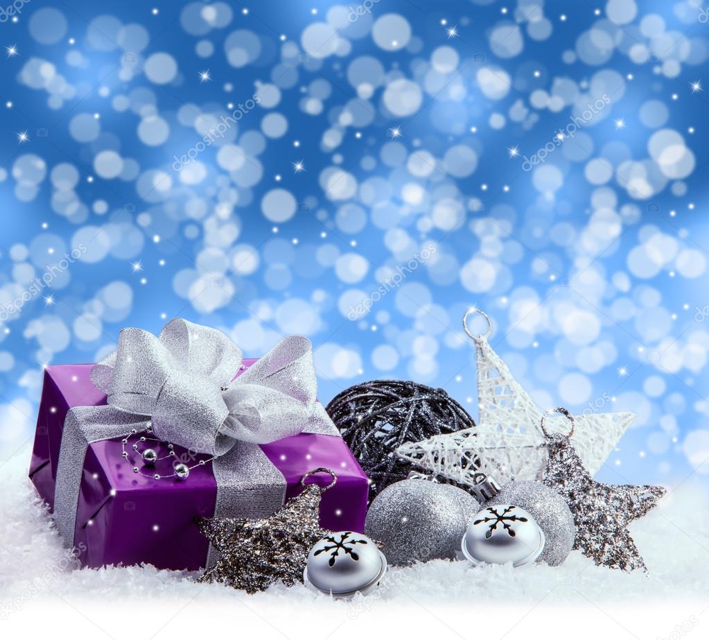 Purple Christmas package , gift of a silver ribbon. Jingle bells , silver christmas balls and christmas stars put on snow. Abstract multicolored blurred background space.