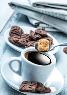 Fincan kahve kaşık şeker kamışı, çikolata bisküvi ve arka plan gazete ile.