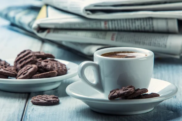 Xícara de café, biscoitos de chocolate e o jornal de fundo . — Fotografia de Stock