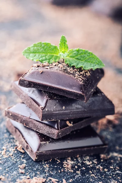 Chocolate. Black chocolate. A few cubes of black chocolate with mint leaves. — Stock Photo, Image