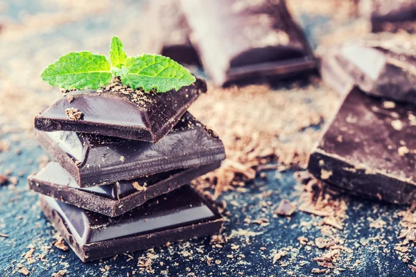 Chocolate. Black chocolate. A few cubes of black chocolate with mint leaves. — Stock Photo, Image