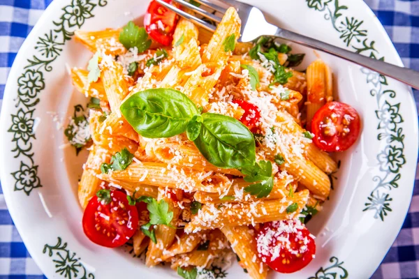 Tallrik med pasta pene Bolognese sås körsbärstomater persilja topp och basilika lämnar på rutig blå duk. — Stockfoto