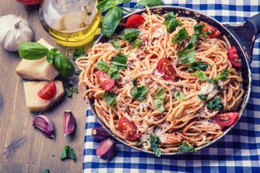 Spagetti bolognese kiraz domates ve fesleğen ile. Mavi kareli masa örtüsü ve rustik ahşap masa domates soslu spagetti