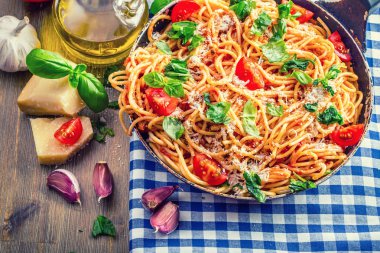 Spagetti bolognese kiraz domates ve fesleğen ile. Mavi kareli masa örtüsü ve rustik ahşap masa domates soslu spagetti