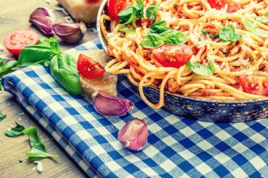 Spagetti bolognese kiraz domates ve fesleğen ile. Mavi kareli masa örtüsü ve rustik ahşap masa domates soslu spagetti