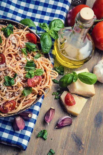 Bolonhesa de espaguete com tomate cereja e manjericão. Espaguete com molho de tomate na toalha de mesa quadriculada azul e mesa de madeira rústica — Fotografia de Stock