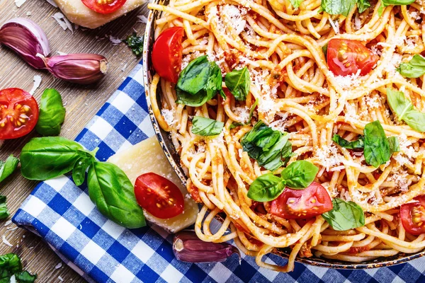 Spagetti bolognese kiraz domates ve fesleğen ile. Mavi kareli masa örtüsü ve rustik ahşap masa domates soslu spagetti — Stok fotoğraf