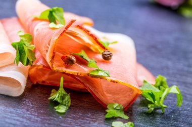 Kıvrılmış dilimleri, Delicious Prosciutto maydanoz ile granit tahta üzerinde yapraklar.