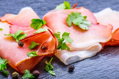 Kıvrılmış dilimleri, Delicious Prosciutto maydanoz ile granit tahta üzerinde yapraklar.