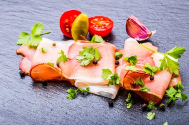 Kıvrılmış dilimleri, Delicious Prosciutto maydanoz ile granit tahta üzerinde yapraklar.