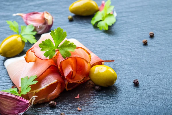 Rodajas rizadas de delicioso jamón con hojas de perejil sobre tabla de granito . —  Fotos de Stock