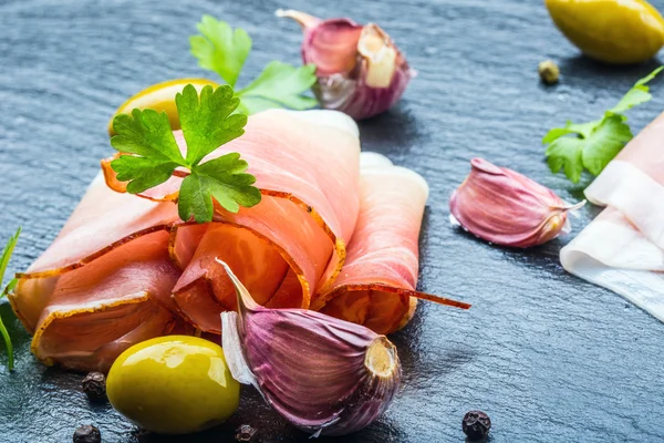 Curled Slices of Delicious Prosciutto with parsley leaves on granite board. — Stock Photo, Image