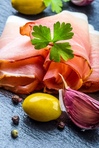 Curled Slices of Delicious Prosciutto with parsley leaves on granite board. — Stock Photo, Image