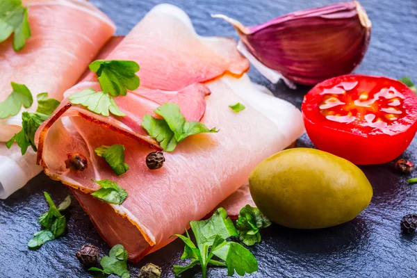 Curled Slices of Delicious Prosciutto with parsley leaves on granite board. — Stock Photo, Image