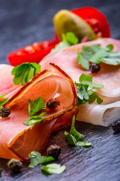 Gekrulde segmenten van Delicious Prosciutto met peterselie bladeren op graniet bord. — Stockfoto