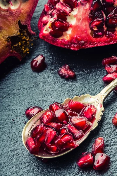 Pieces and grains of ripe pomegranate. Pomegranate seeds. Part of pomegranate fruit on granite board and antique spoon.