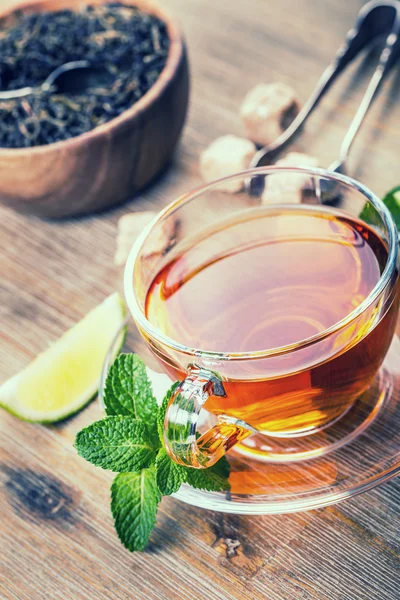 Tea in a glass cup, mint leaves, dried tea, sliced lime — Stock Photo, Image