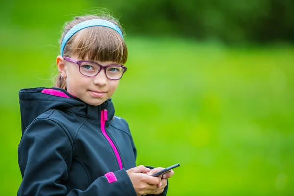 Portre küçük kız cep telefonu ile kapatın. Ayakta ve manifatura telefon ile küçük kız — Stok fotoğraf