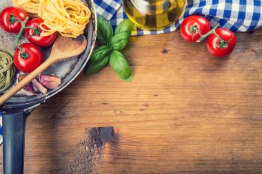 Italian and Mediterranean food ingredients on wooden background.Cherry tomatoes pasta, basil leaves and carafe with olive oil.
