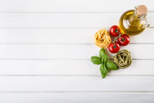 Zutaten italienischer und mediterraner Küche auf hölzernem Hintergrund. Kirschtomaten, Pasta, Basilikumblätter und Karaffe mit Olivenöl. — Stockfoto