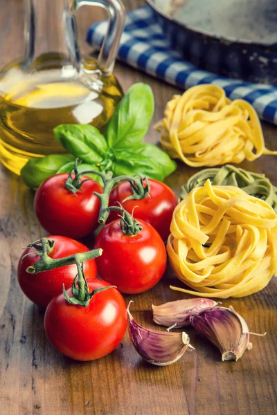 Zutaten italienischer und mediterraner Küche auf hölzernem Hintergrund. Kirschtomaten, Pasta, Basilikumblätter und Karaffe mit Olivenöl. — Stockfoto