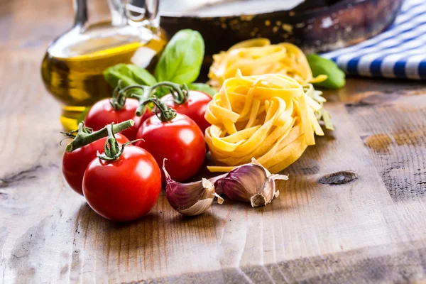 Zutaten italienischer und mediterraner Küche auf hölzernem Hintergrund. Kirschtomaten, Pasta, Basilikumblätter und Karaffe mit Olivenöl. — Stockfoto