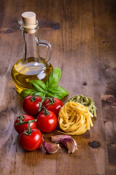 Итальянские и средиземноморские продукты питания на деревянном фоне. Черри помидоры паста, листья базилика и графин с оливковым маслом . — стоковое фото