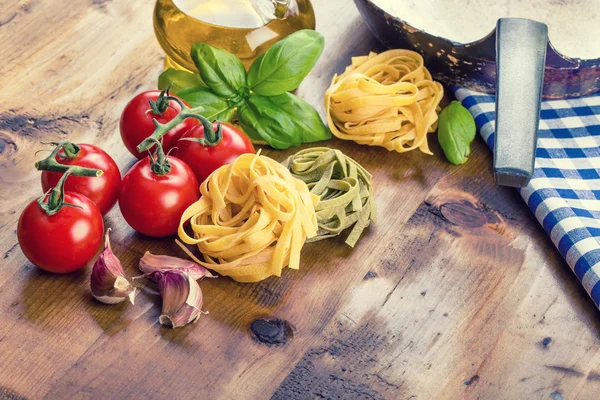 Zutaten italienischer und mediterraner Küche auf hölzernem Hintergrund. Kirschtomaten, Pasta, Basilikumblätter und Karaffe mit Olivenöl. — Stockfoto
