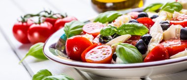 Caprese. Caprese salad. Italian salad. Mediterranean salad. Italian cuisine. Mediterranean cuisine. Tomato mozzarella basil leaves black olives and olive oil on wooden table.