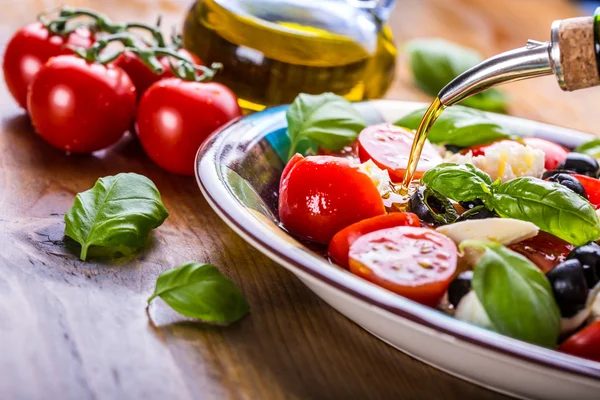 Caprese. Salată Caprese. Salată italiană. Salată mediteraneană. Bucătărie italiană. Bucătărie mediteraneană. Roșii mozzarella busuioc frunze măsline negre și ulei de măsline pe masă de lemn . — Fotografie, imagine de stoc