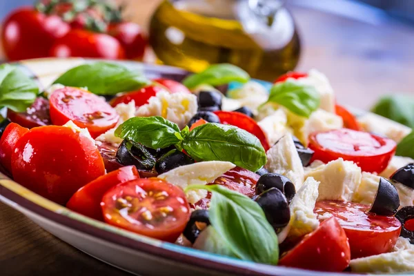 Caprese. Salada Caprese. Salada italiana. Salada mediterrânea. Cozinha italiana. Cozinha mediterrânea. Tomate mussarela manjericão folhas azeitonas pretas e azeite sobre mesa de madeira . — Fotografia de Stock