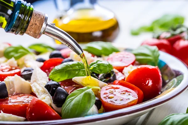 Caprese. Caprese salad. Italian salad. Mediterranean salad. Italian cuisine. Mediterranean cuisine. Tomato mozzarella basil leaves black olives and olive oil on wooden table. — Zdjęcie stockowe