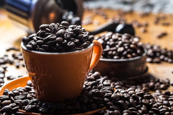 Kawy. Ziarna kawy. Palonych ziaren kawy rozlane swobodnie na drewnianym stole. Kawa w naczyniu do zmielonej kawy. — Zdjęcie stockowe